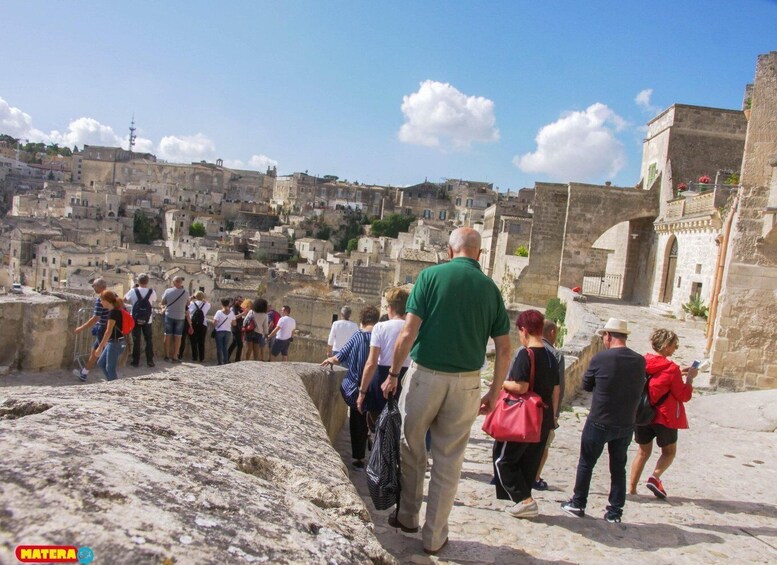 A group of tourists walking along a stone pathway in a historic town with old buildings and a stone wall. 1