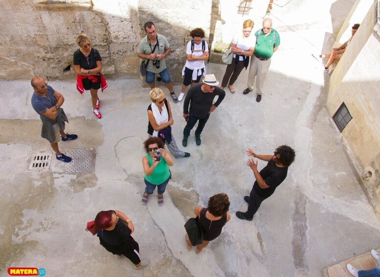 A group of people standing in a courtyard with stone walls and a drain. 2
