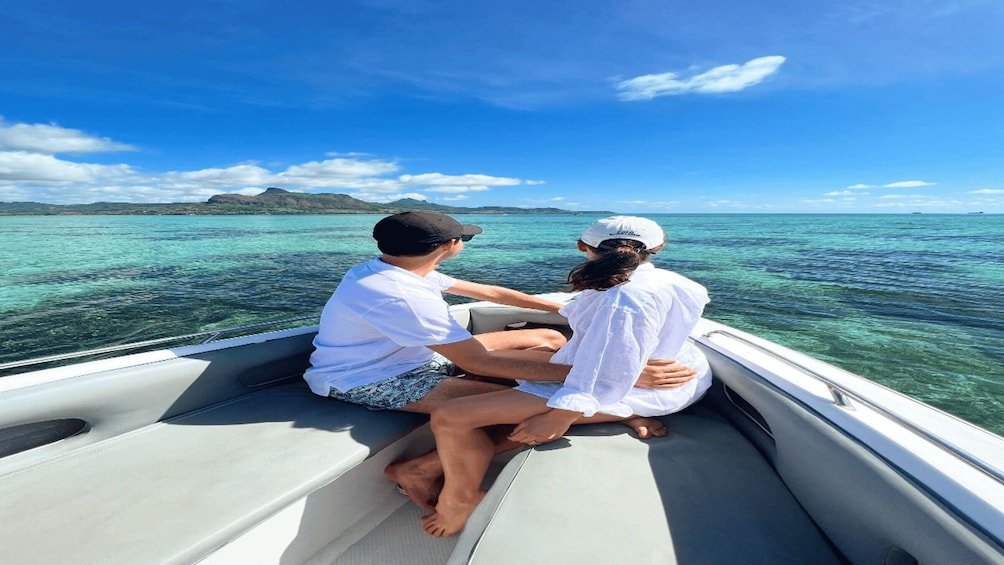 A boat with two people sitting on the back, a clear blue sky, and turquoise water. 1
