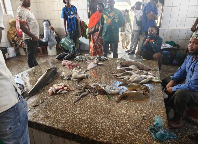 Ein Marktgeschehen mit Personen und verschiedenen Fischen, die auf einer Theke ausliegen. 3