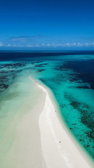A white sandy beach with clear turquoise waters and a line of people walking along the shore. 1