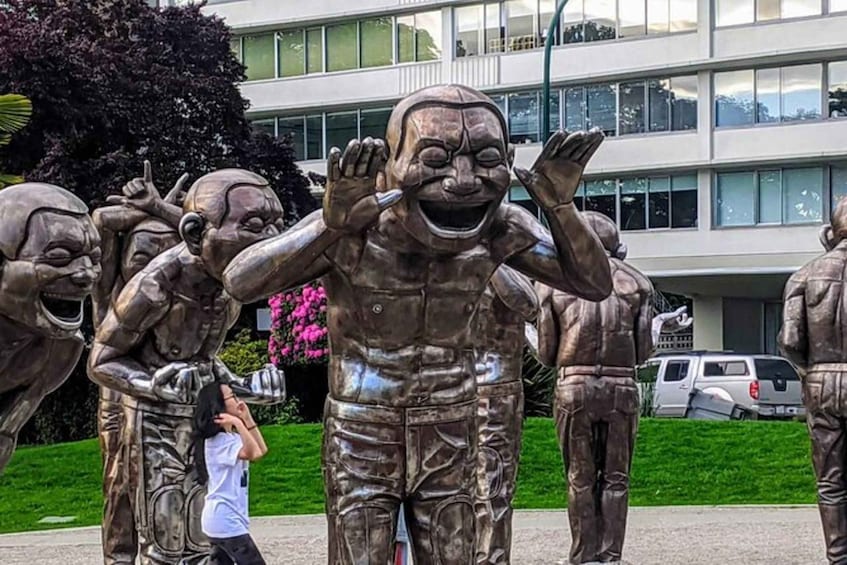 A group of bronze statues of people in various poses, with a building and cars in the background. 2