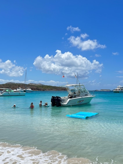 A boat with a red flag, people swimming, and a clear blue sky. 4