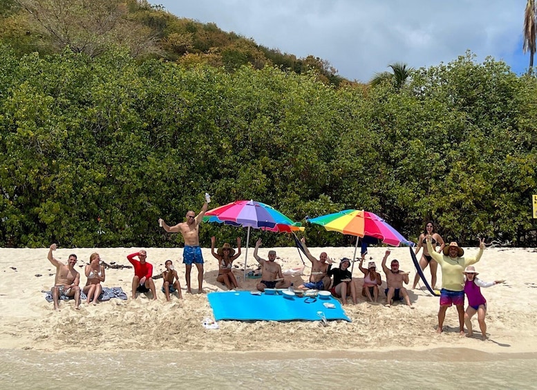 A group of people on a sandy beach with colorful umbrellas and a blue mat. 3