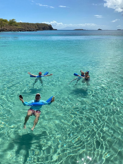 Three people floating in clear turquoise water, using blue floatation devices. 2
