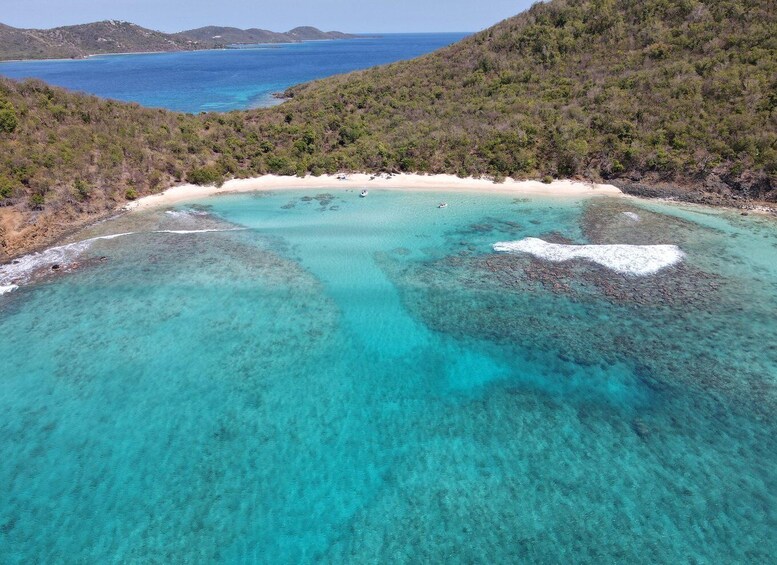 A turquoise lagoon with white sand beaches and rocky outcrops, surrounded by dense green hills. 1