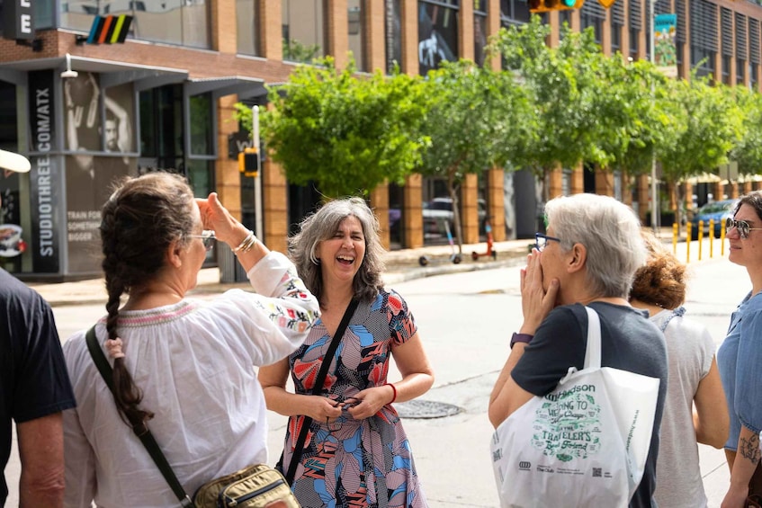 A group of people on a city street with buildings, trees, and traffic lights. 1