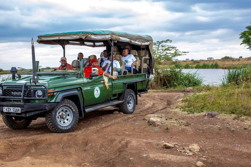 Un Toyota Land Cruiser verde con passeggeri su un sentiero sterrato vicino all'acqua. 1