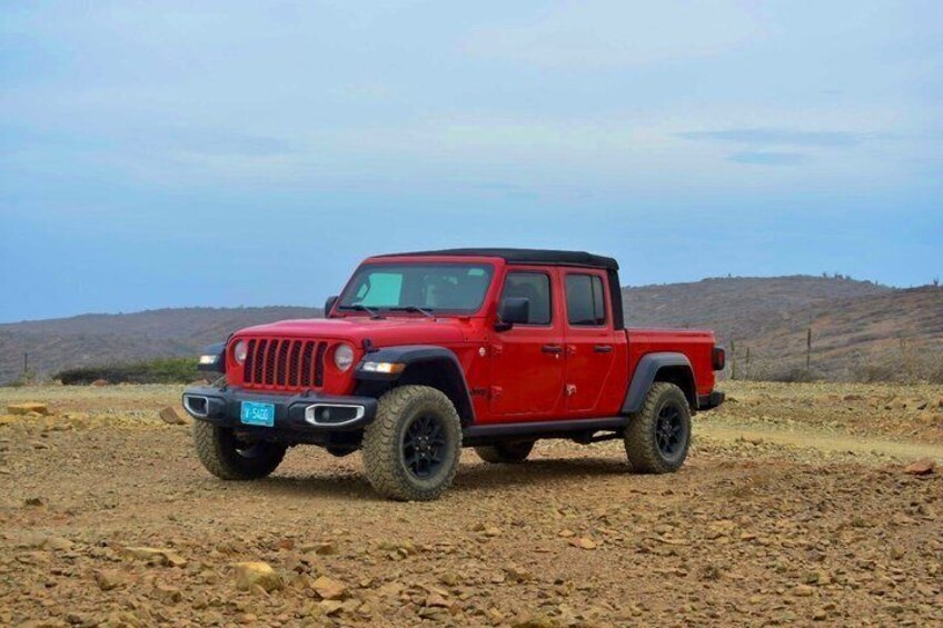 A red off-road vehicle parked on a dirt road with a hilly landscape in the background. 3