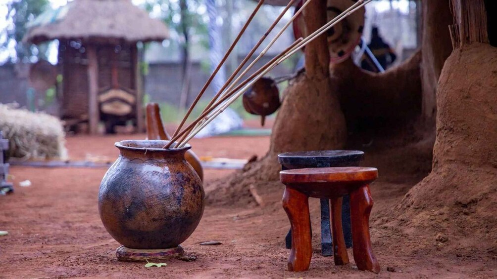 Un décor extérieur rustique comprenant un pot en métal, un tabouret en bois et une structure recouverte de chaume. 4