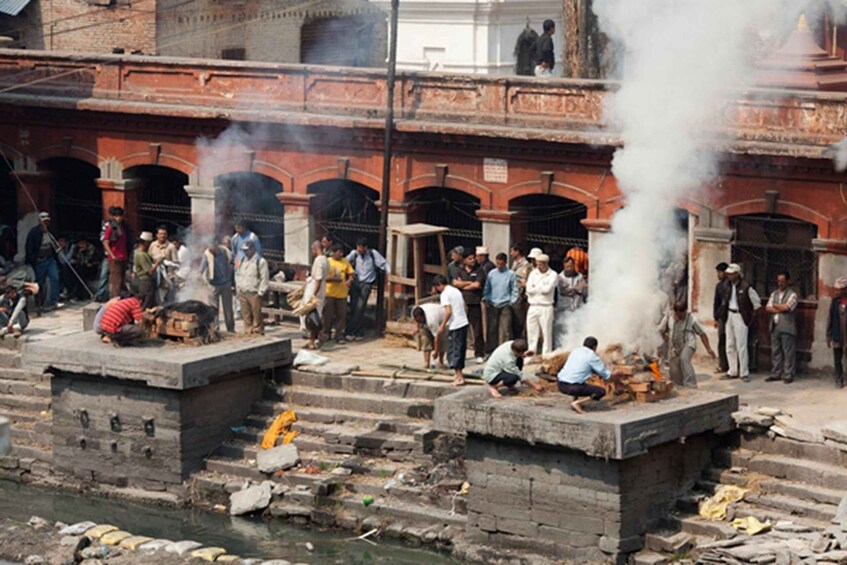 A group of people near a riverbank with smoke rising from a structure. 3