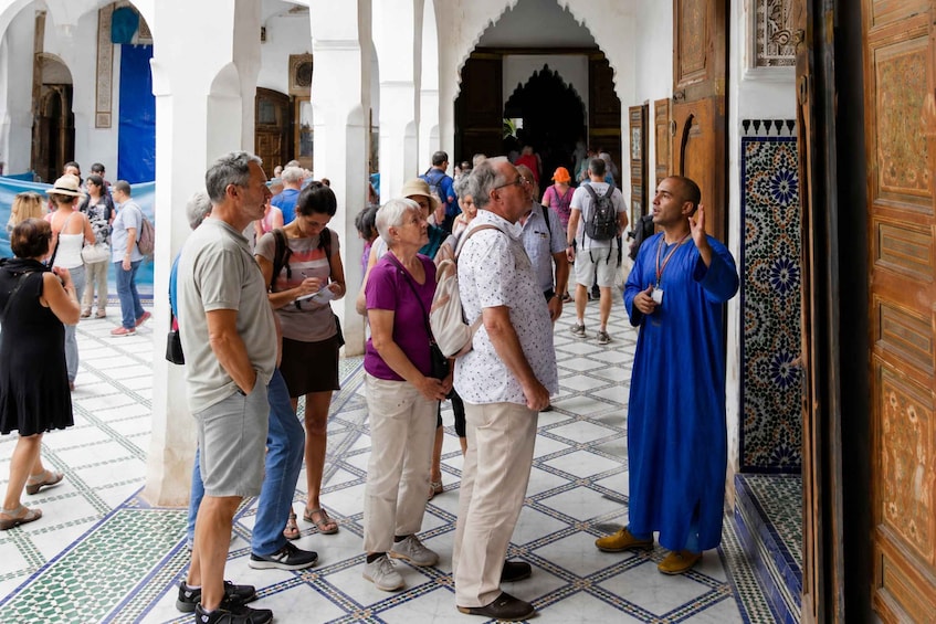 A group of people standing in a courtyard with tiled flooring and ornate wooden doors. 1