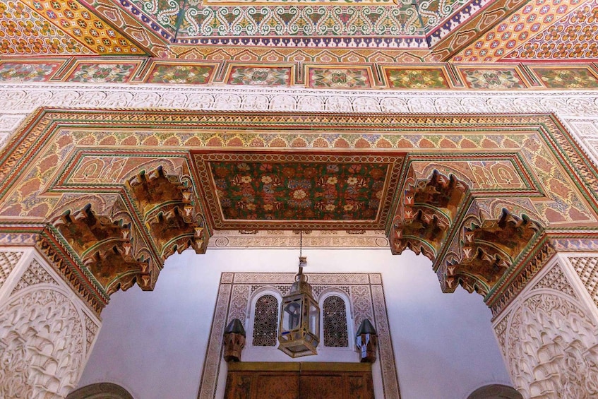 An ornate ceiling with intricate geometric and floral patterns, a hanging lantern, and detailed stucco work. 2