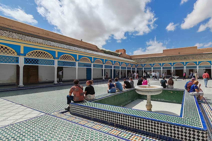 A courtyard with tiled floors, a fountain, and people sitting and walking. 3