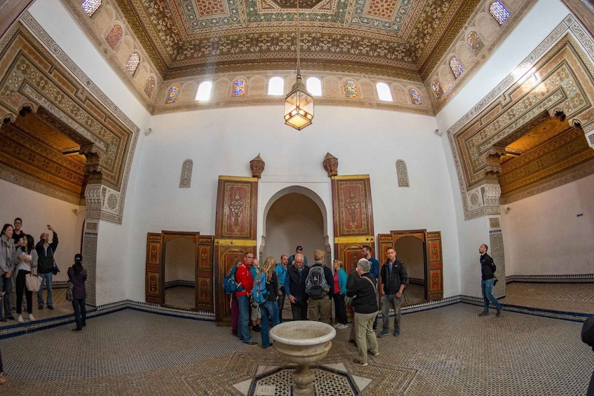 An ornate interior with intricate tile work, a central fountain, and a group of people observing. 5