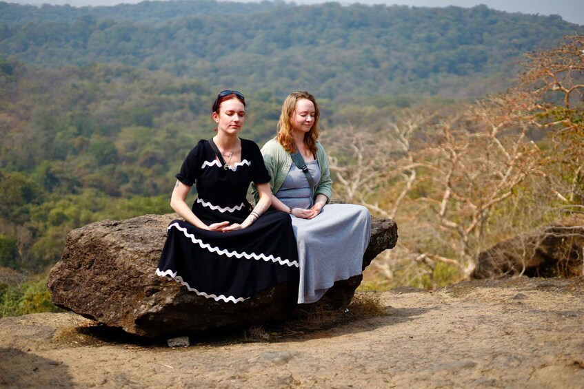 Two women sitting on a rock with a forested landscape in the background. 1