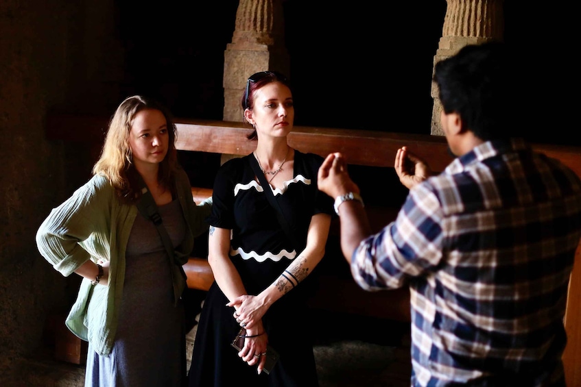 Three people in a dimly lit room with stone columns. 1