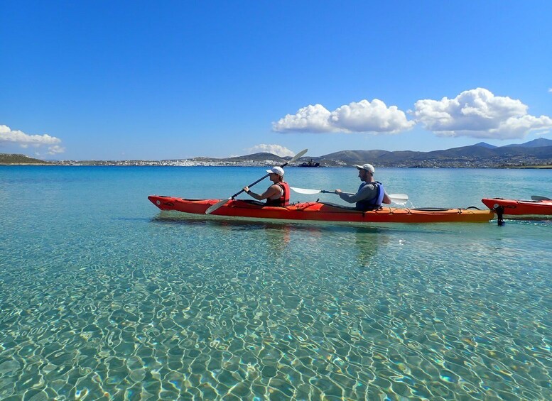 Two people kayaking on a clear blue sea with mountains in the background. 1