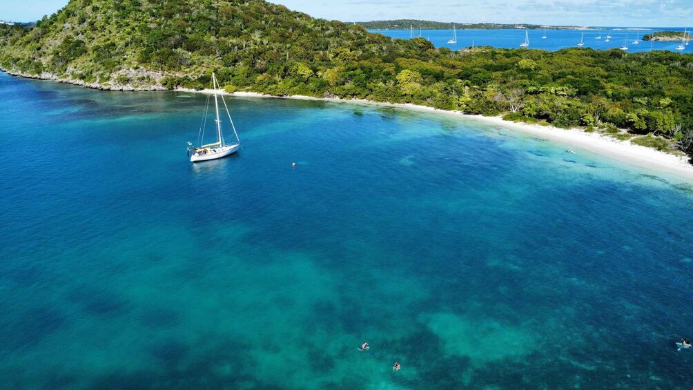 A sailboat on a turquoise sea, a white sandy beach, and a forested hill. 4