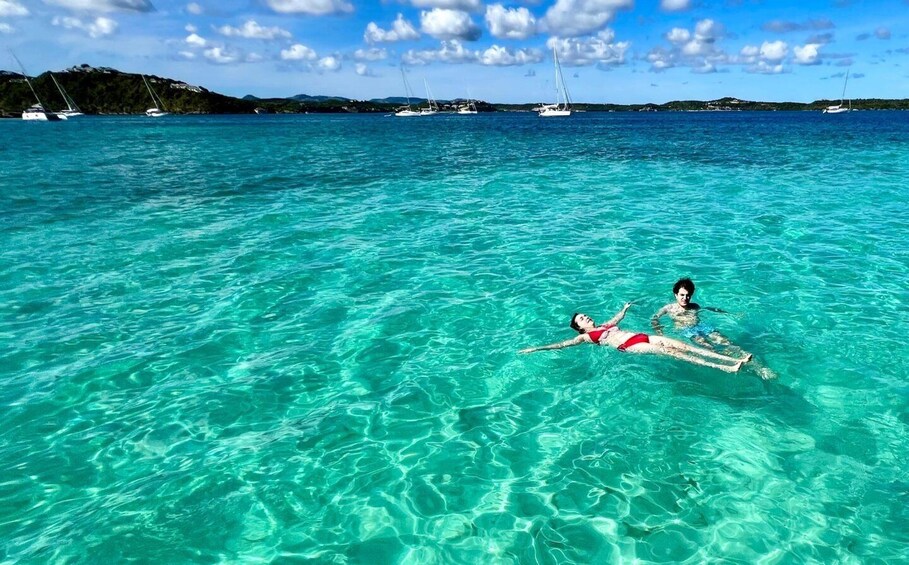 Two people floating on a turquoise sea with boats in the background. 5