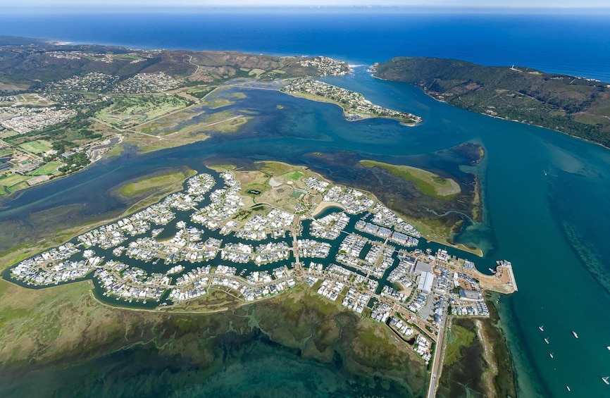 An aerial view of a coastal residential area with a marina, surrounded by water bodies and hilly terrain. 1