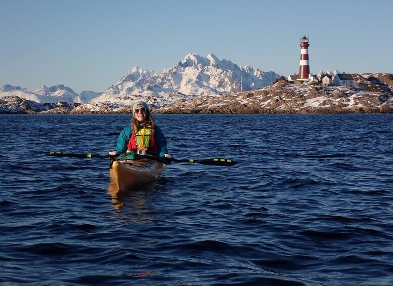 A person kayaking on a body of water with a lighthouse and snow-covered mountains in the background. 3