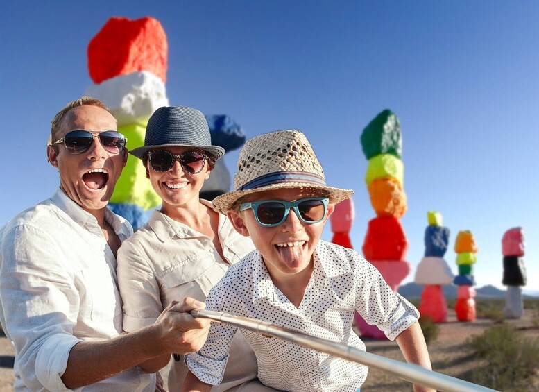 Three people in a desert with colorful sculptures in the background. 5