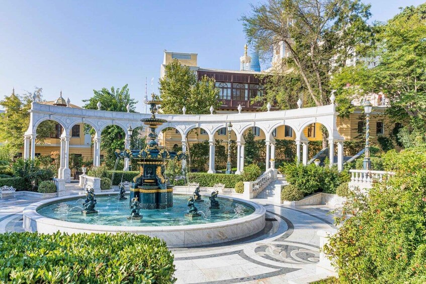 A classical fountain with statues in a courtyard surrounded by white columns and greenery. 1