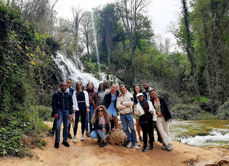 A group of people standing in front of a waterfall surrounded by trees. 4