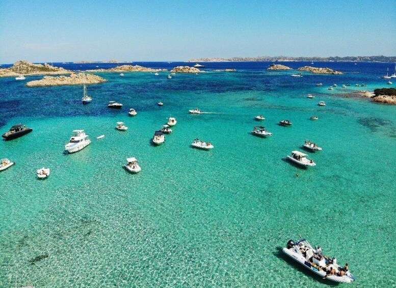 A turquoise sea with numerous boats, rocky outcrops, and a clear sky. 2