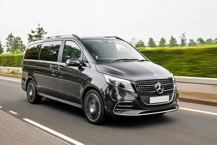 A black Mercedes-Benz minivan driving on a highway with greenery in the background. 3