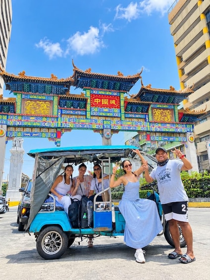 Un grupo de personas en un tuk-tuk, con un arco tradicional chino al fondo. 1