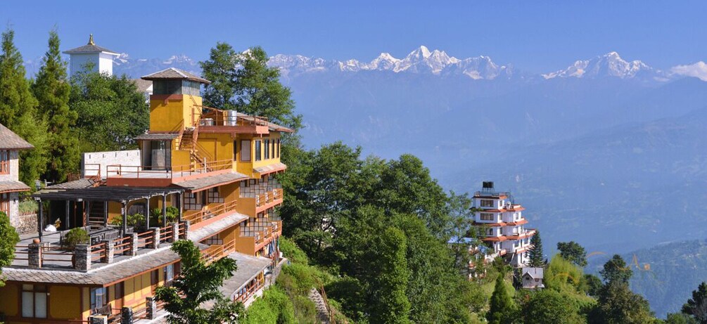A mountain resort with multi-story buildings, a water tower, and snow-capped peaks in the background. 5