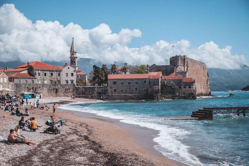 Eine Küstenstadt mit einer markanten Kirche, einer Festung und einem Strand, an dem sich Menschen entspannen. 5