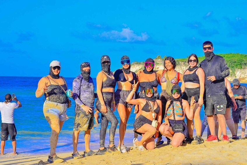 A group of people on a beach with clear blue water and a rocky coastline in the background. 5