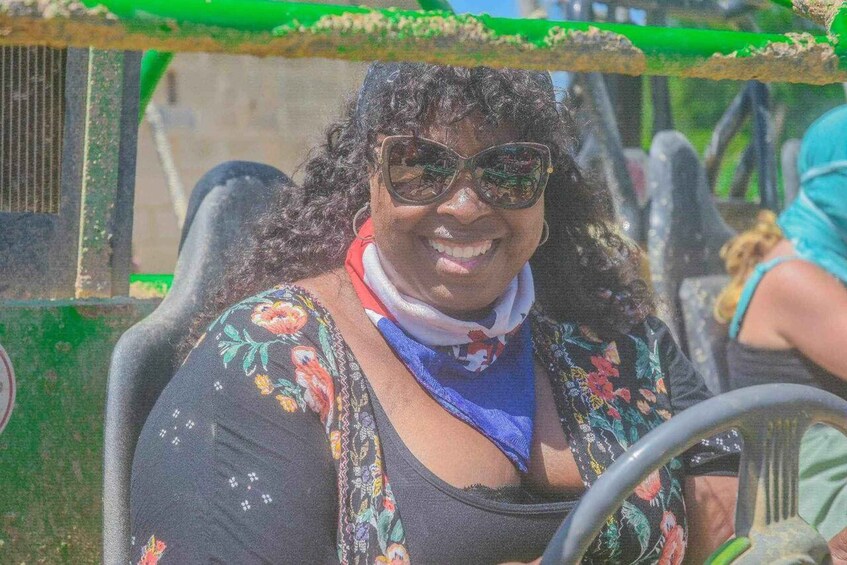 A person driving a vehicle with a floral-patterned top and a blue scarf. 4