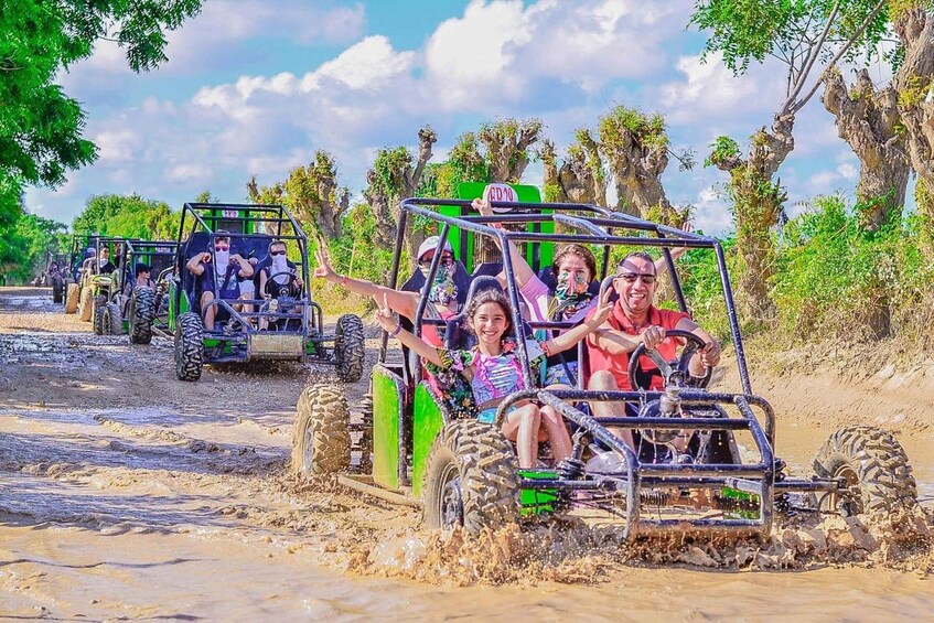 People riding off-road vehicles on a muddy path surrounded by trees. 1