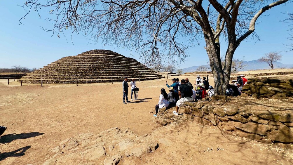 A large terraced structure in a dry, open landscape with a group of people observing it. 4