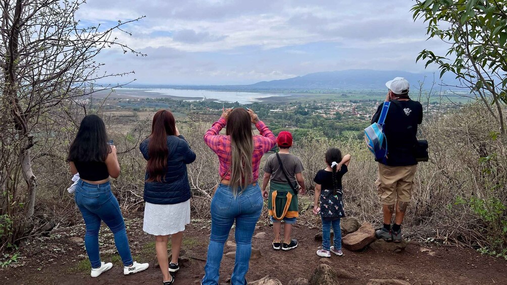 A group of people standing on a rocky outcrop overlooking a valley with a body of water and distant mountains. 5