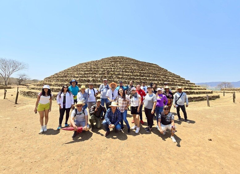 A group of people posing in front of a large pyramid-like structure in a desert landscape. 5
