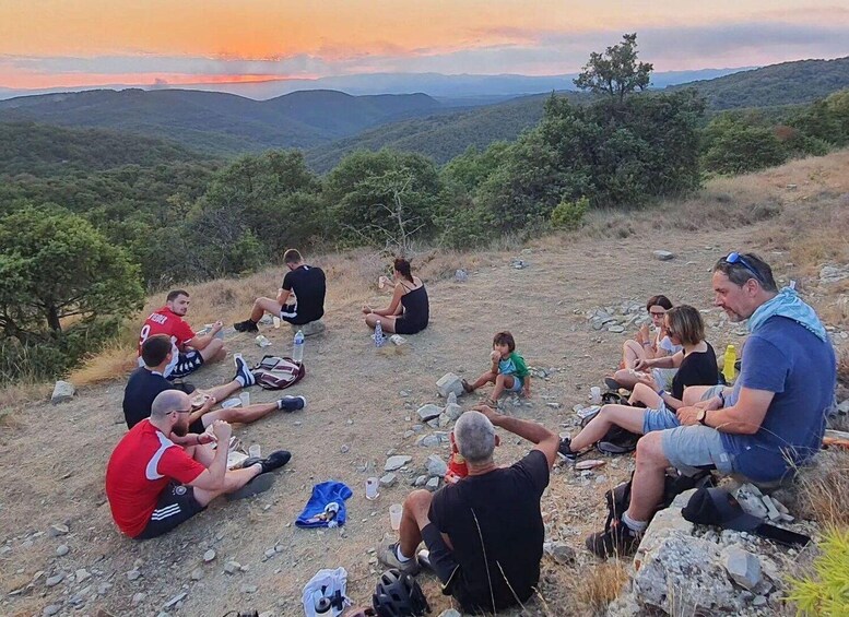 A group of people sitting on a rocky hillside during sunset. 1