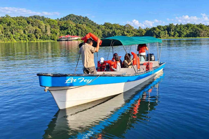 A boat named 'La Fey' on calm water with passengers wearing life jackets, surrounded by lush greenery and a clear sky. 5