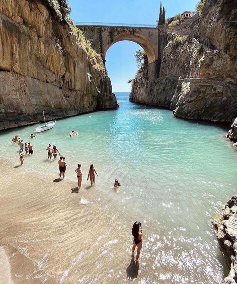 Paisaje costero con un puente, agua turquesa cristalina y gente nadando y paseando por la playa. 5