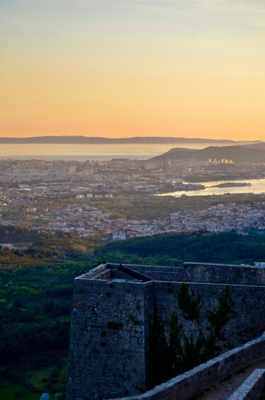 Un paisaje urbano costero al atardecer con una imponente fortaleza de piedra en primer plano. 5