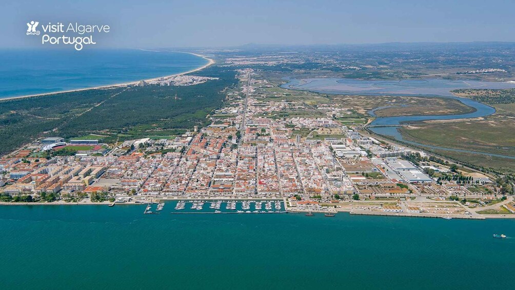 An aerial view of a coastal city with a dense urban area, a marina with boats, and a coastline with a beach and water bodies. 3