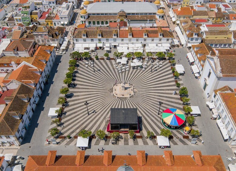 An aerial view of a square with a central monument, surrounded by buildings with red-tiled roofs. 2