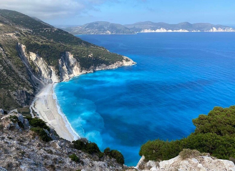A coastal landscape with a beach, cliffs, and a clear blue sea. 1