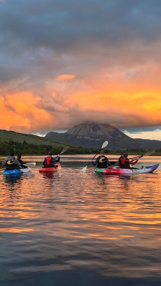Trois personnes pratiquant le kayak sur un lac paisible, avec une montagne en arrière-plan, au coucher du soleil. 1