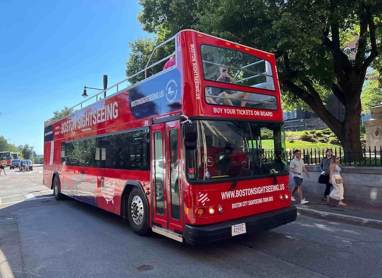 A red double-decker bus with "Boston Sightseeing" and "www.boston-sightseeing.us" on its side, parked on a street. 3
