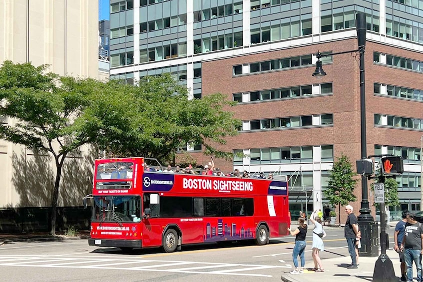 A red double-decker bus with "BOSTON SIGHTSEEING" on the side, parked at a traffic light with people standing nearby. 5